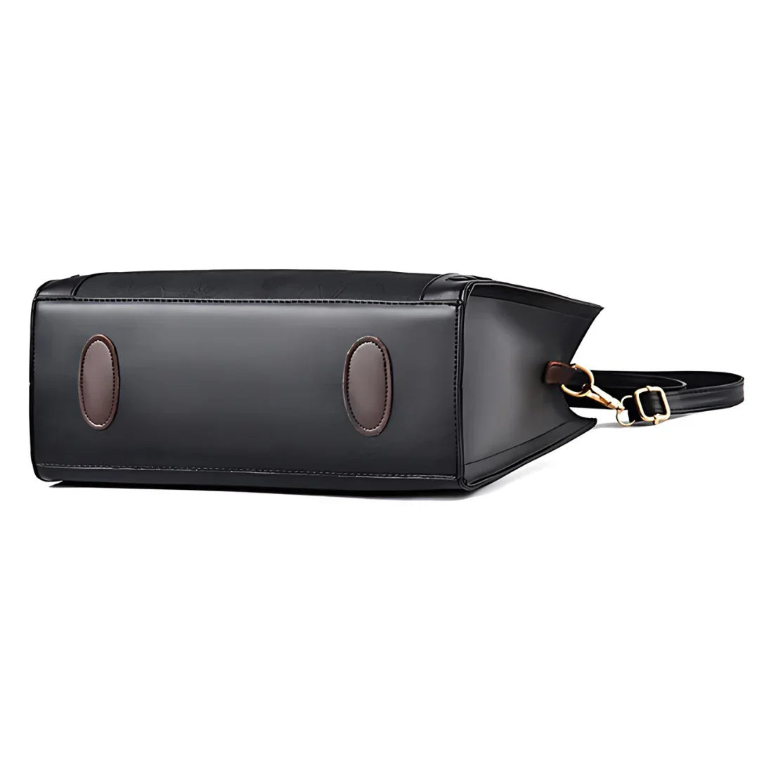 Black leather tote bag bottom view with brown oval feet and gold buckle strap