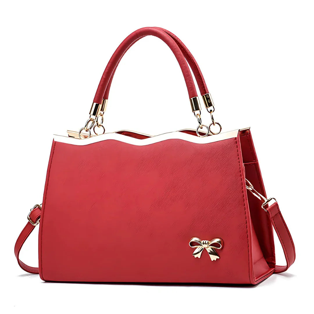 Red handbag with gold bow ornament, top handles, and detachable shoulder strap on white background