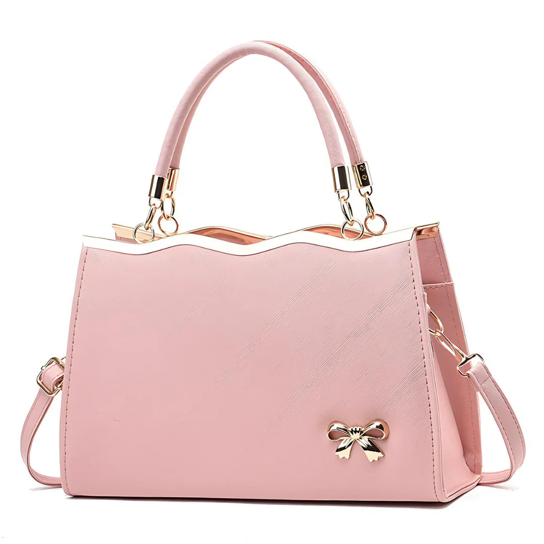 Pink handbag with gold bow charm, dual handles, shoulder strap, and wavy top edge