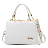 White leather handbag with gold hardware, bow detail, top handles, and shoulder strap