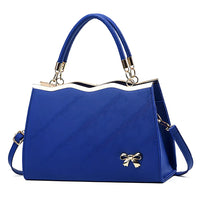 Elegant blue handbag with gold bow accent and wave edge design, detachable strap
