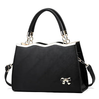Elegant black handbag with gold trim, two handles, and a small gold bow accent