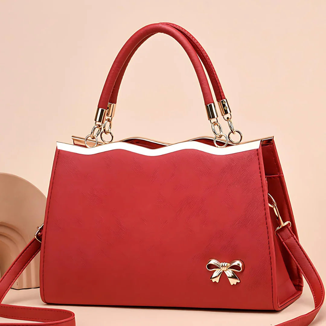 Red handbag with gold accents and bow detail, elegant purse on beige background