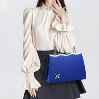 Woman in cream blouse holding elegant blue handbag with gold bow charm
