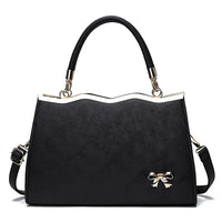 Elegant black handbag with gold handle accents and bow detail on white background