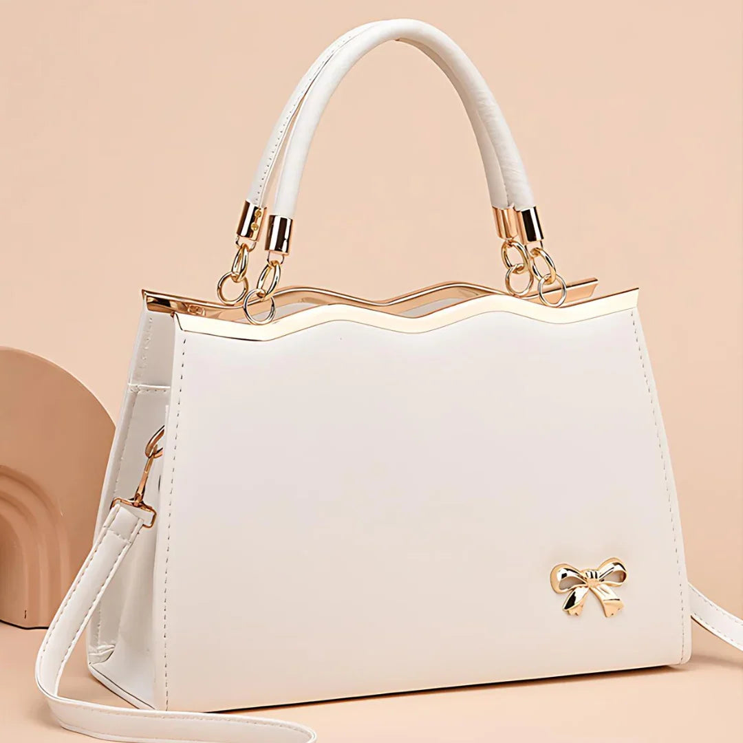 White handbag with gold accents and a bow detail on a beige background