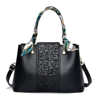 Black leather handbag with embossed floral pattern, printed scarf handles, and gold accents