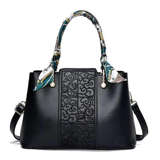 Black leather handbag with embossed floral pattern, printed scarf handles, and gold accents
