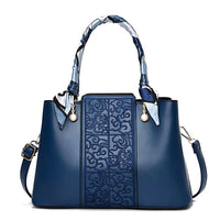 Elegant blue leather handbag with embossed pattern, scarf-wrapped handle, and gold accents