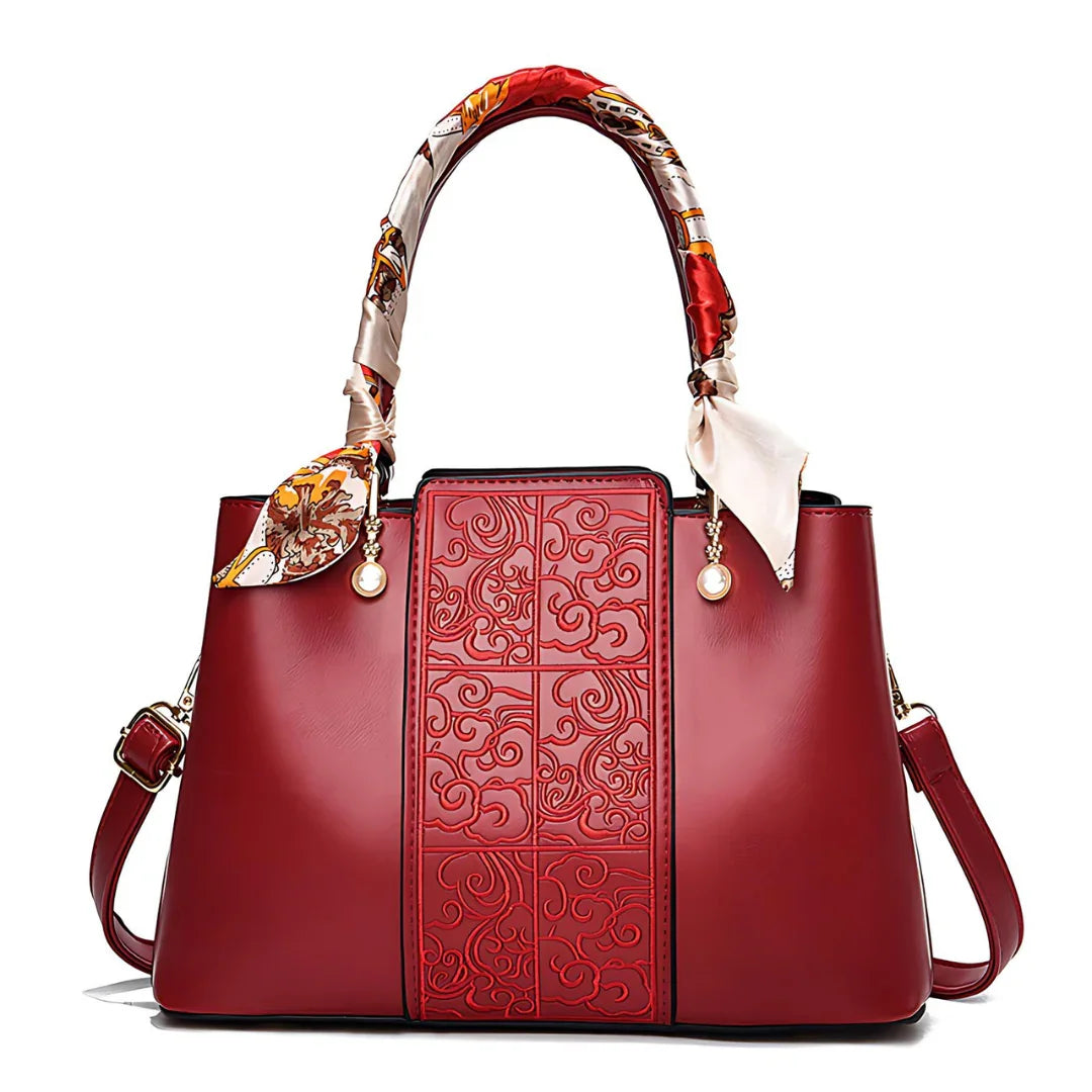 Elegant red leather handbag with embossed pattern, silk scarf handle, and gold pearl accents