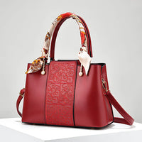 Elegant red handbag with embossed pattern, silk scarf handle, and detachable strap