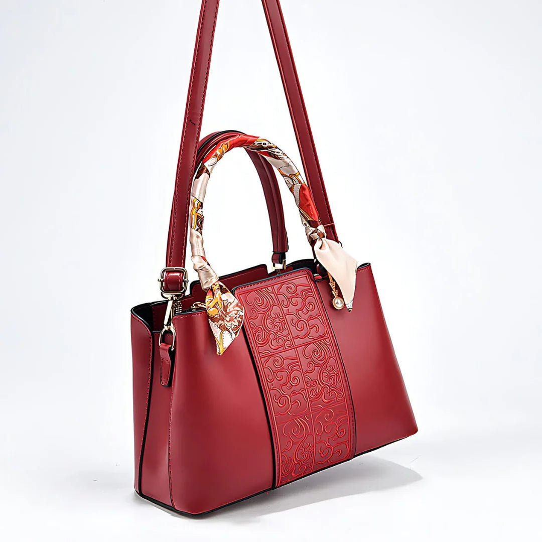 Red leather handbag with embossed pattern, decorative scarf handles, and shoulder strap