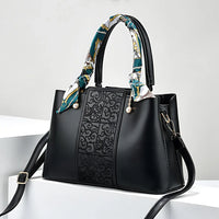 Black leather handbag with embossed front panel, patterned handle scarf, and gold hardware