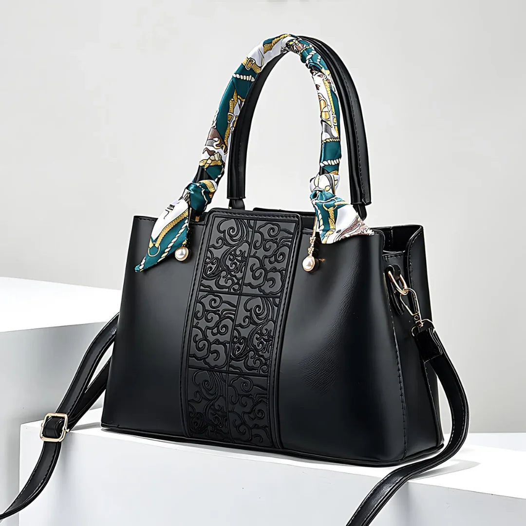 Black leather handbag with embossed front panel, patterned handle scarf, and gold hardware