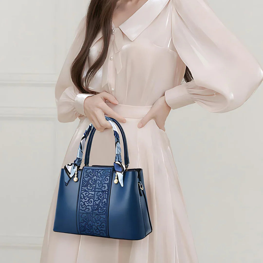 Woman in pale pink dress holding elegant blue leather handbag with patterned details