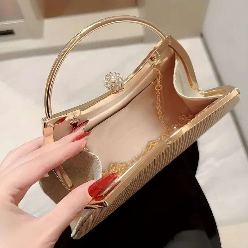 Gold metal frame clutch handbag with chain strap and crystal clasp, held by manicured hand