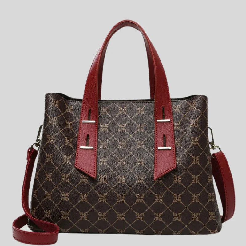 Brown handbag with geometric pattern, red leather handles and strap, on gray background