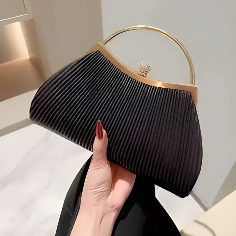 Elegant black pleated handbag with gold handle held indoors, modern fashion accessory