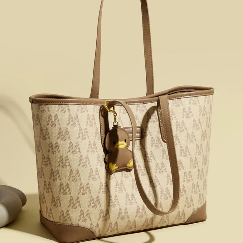 Beige and brown tote bag with M pattern and duck keychain accessory on neutral background