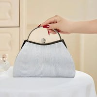 Elegant silver evening handbag with top handle, held by hand on a white table