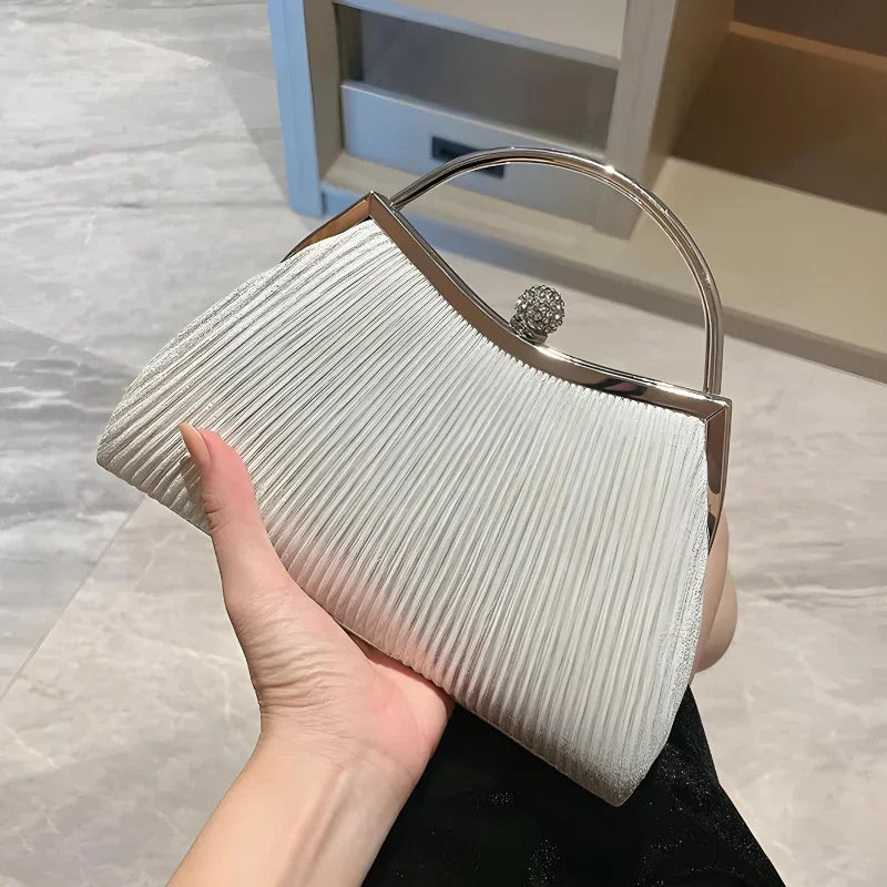 Elegant white pleated evening clutch bag with silver handle, held indoors