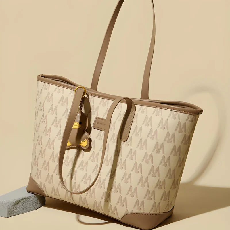 Beige designer tote bag with high heel print, tan leather trim, and yellow keychain charm