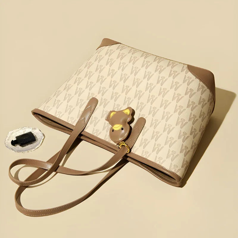 Beige and brown designer tote bag with V pattern and bear keychain on neutral background