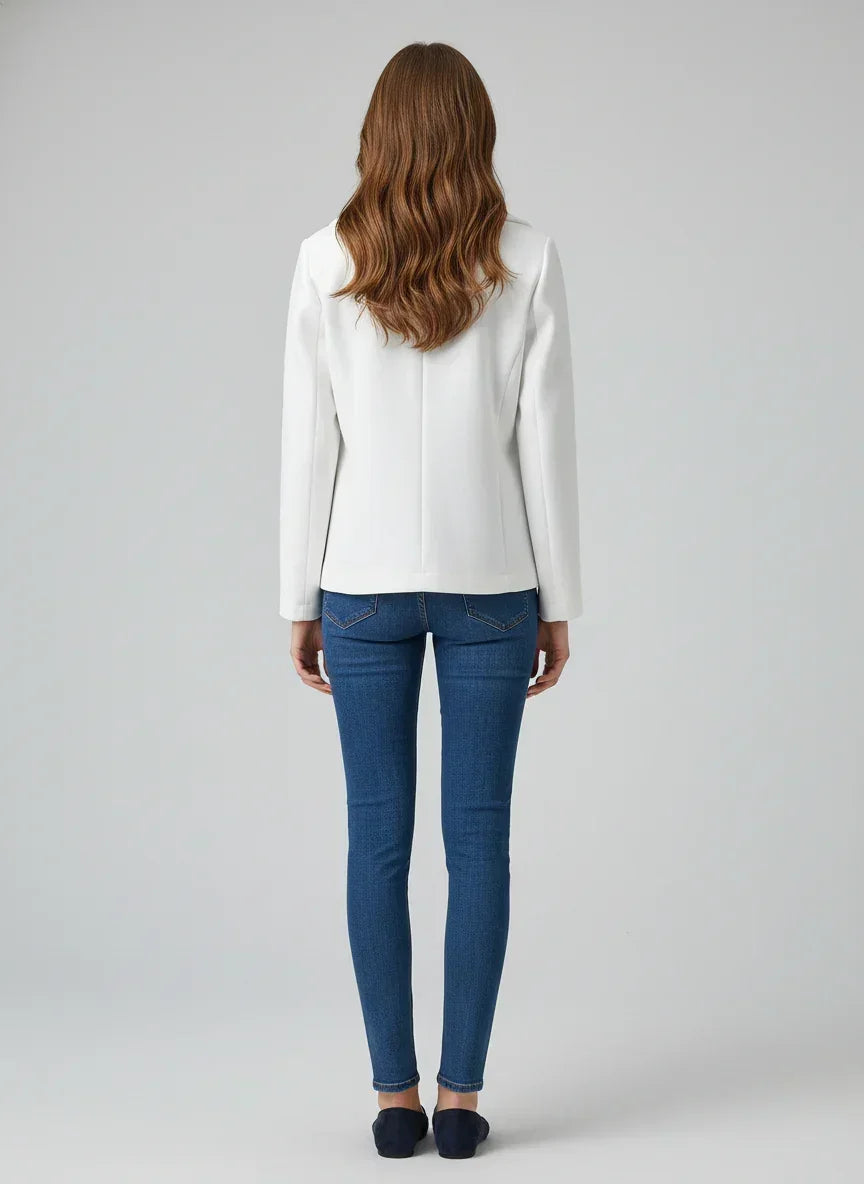 Person wearing a white blazer and blue jeans on a gray background
