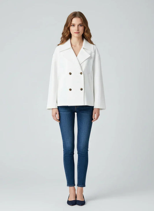 Woman wearing a white coat with gold buttons and blue jeans on a light gray background