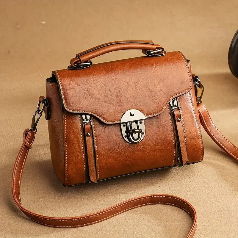 Brown leather crossbody bag with top handle and metal lock on tan background