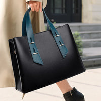 Woman holding black leather tote bag with teal handles, street style fashion accessory