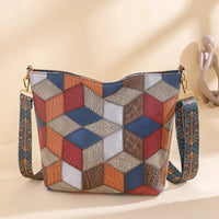 Geometric patchwork shoulder bag with colorful cube pattern and decorative strap on beige surface
