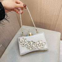 Hand holding a silver clutch purse with rhinestone embellishments and a gold clasp handle