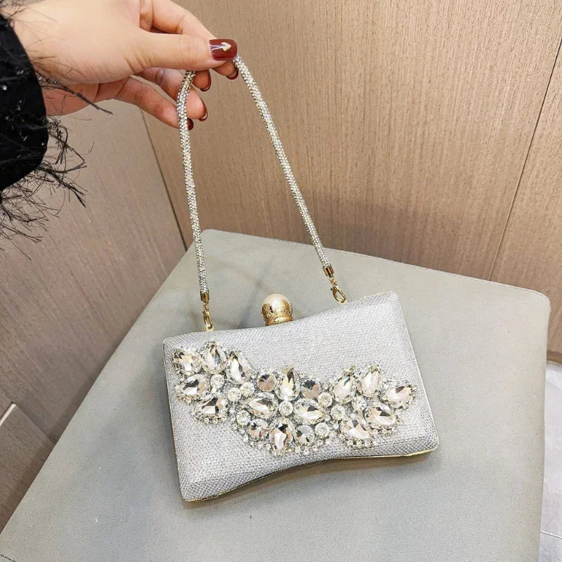 Hand holding a silver clutch purse with rhinestone embellishments and a gold clasp handle