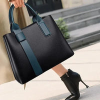 Woman carrying black leather tote bag with blue handles, wearing black high heel boots