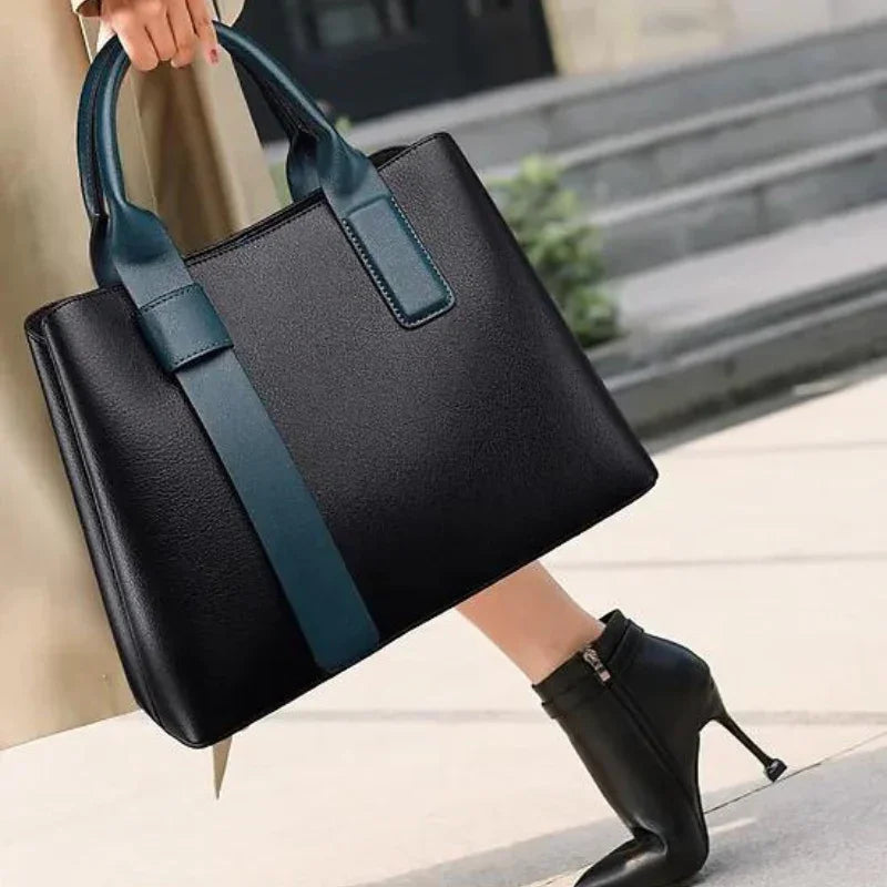 Woman carrying black leather tote bag with blue handles, wearing black high heel boots