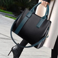 Black leather tote bag with teal handles and shoulder strap, held by woman in high heels