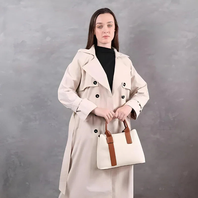 Woman in beige trench coat holding a white handbag with brown straps, grey background