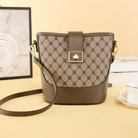 Brown leather crossbody bag with geometric pattern, gold buckle, on beige table