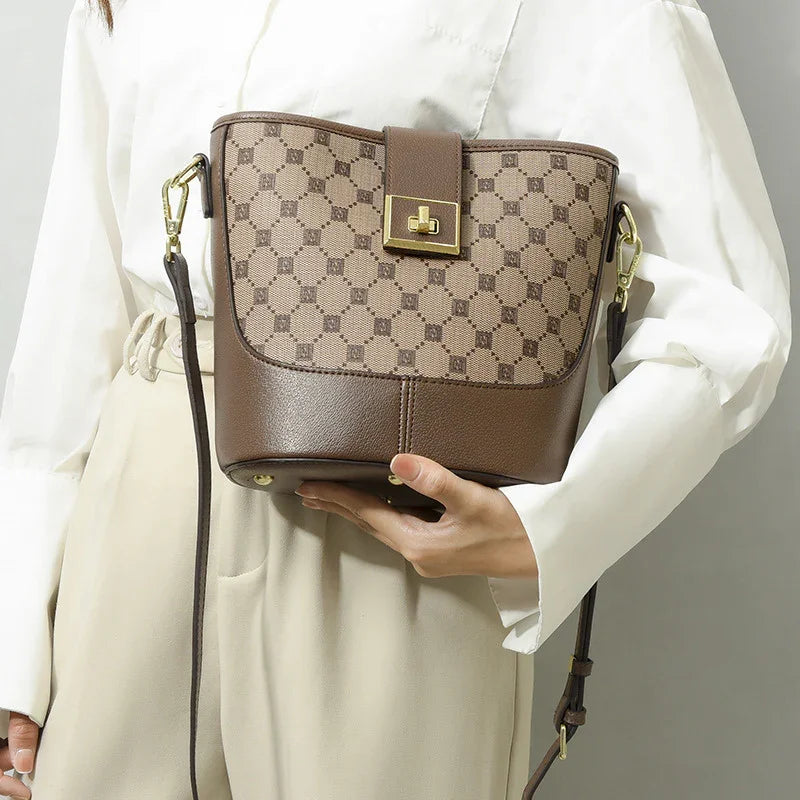 Woman holding brown designer crossbody bucket bag with gold hardware and geometric pattern