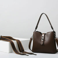 Brown leather shoulder bag with adjustable strap on white minimalist background